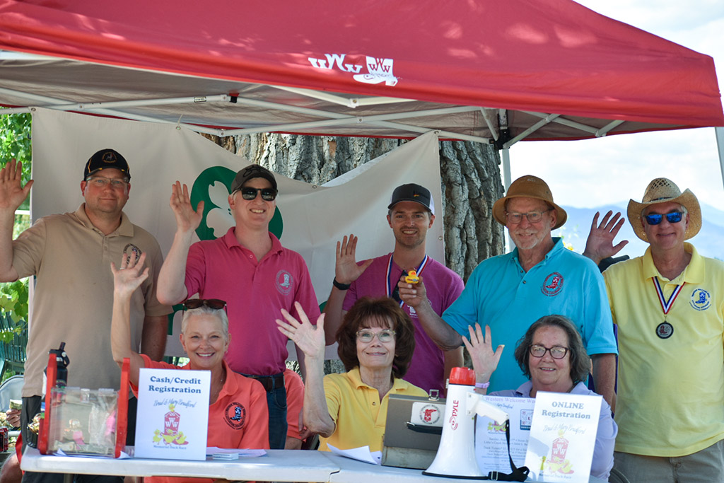 Group of people under a small red canopy waving to the camera.